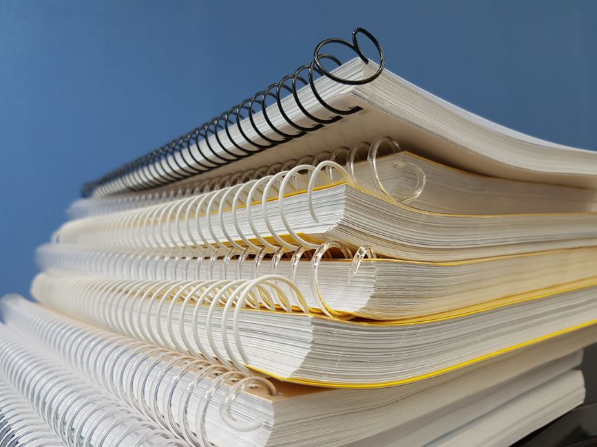 spring-notebook-book-perspective-159682-159682-1 Close-up of stacked spiral notebooks with varied bindings against a blue backdrop.